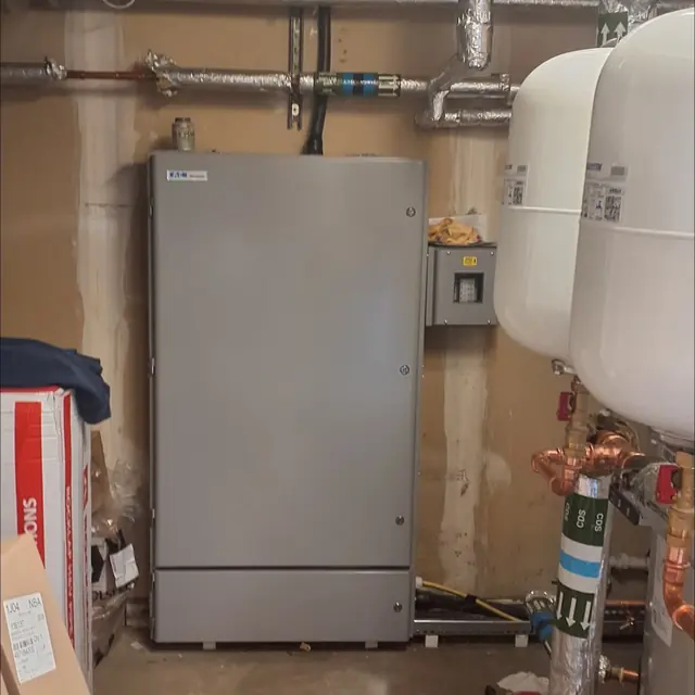 Finished commercial distribution board in a grey steel cabinet, closed up in a plant room beside pipework and water tanks