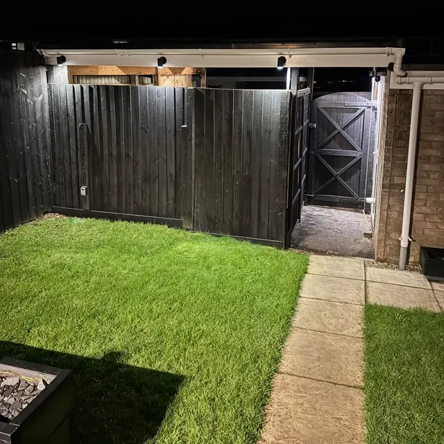 Downlights along a garden fence lighting the lawn and side gate at night